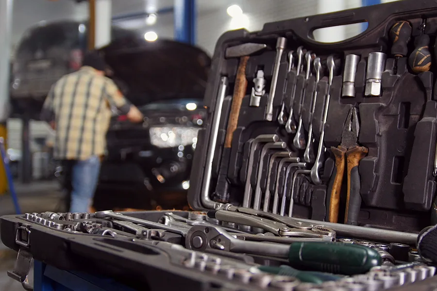 A case of repair tools in the foreground will an auto mechanic works on a car in the background