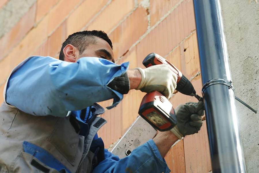 Workman installing a heavy-duty gutter downspout on the side of a building